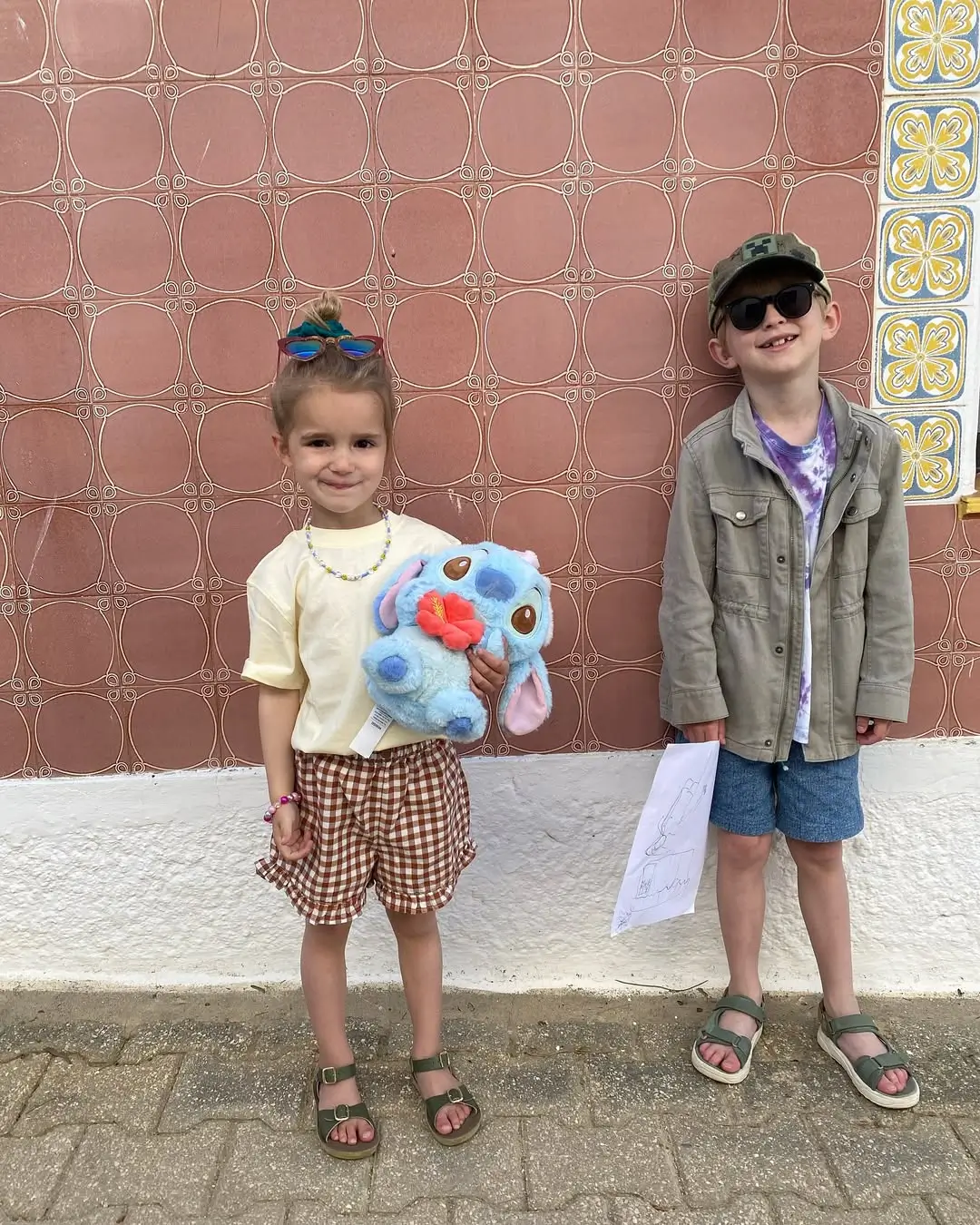 duas crianças de férias com roupa fixe, colorida e a agarrar um peluche