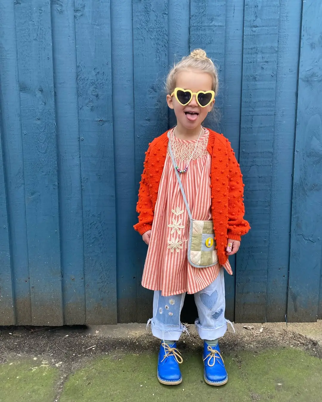 rapariga cheia de estilo e roupa colorida calças de ganga e casaco encarnado sapatos azuis e bibe encarnado as riscas e oculos de sol corações amarelos